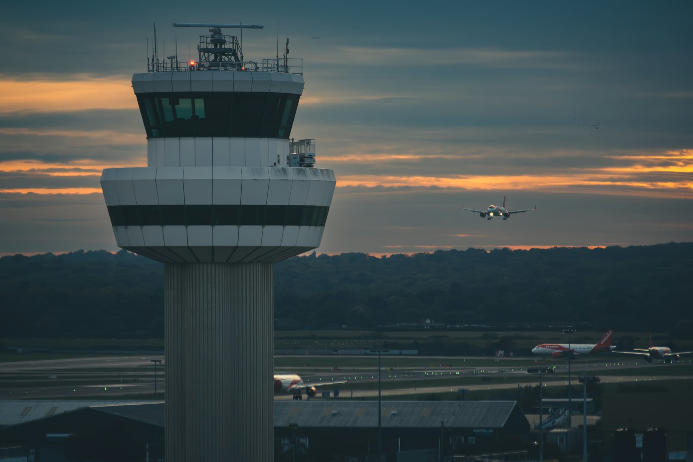 Gatwick Airport control tower at sunset with aircraft on approach
